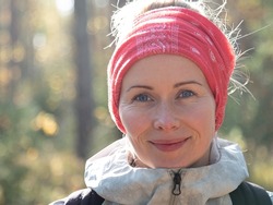 A beautiful white woman with a scarf on her head alone in the woods smiles at the camera. Sunlight shines on a woman's face. Soft focus