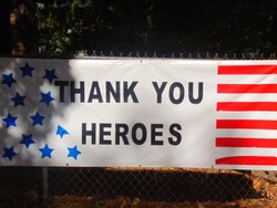 Stars and Stripes banner thanking the military and first responder heroes hanging from a fence