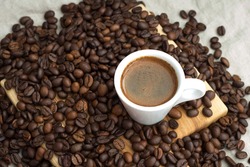 A cup of coffee among selected and calibrated Arabica coffee beans scattered on a napkin, table, blended, top view