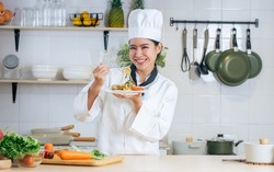Portrait beautiful Asian professional female chef wearing white uniform, hat, showing plate of spaghetti, cooking in kitchen, making surprising face with happiness. Restaurant, Food Concept