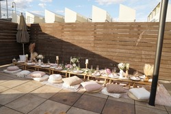 A table is set up for a fancy picnic on top of a residential rooftop with pillow cushions and nice plates, utensils and stemware
