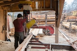 A worker works on sawmill equipment. Wood processing work process. Timber industry.