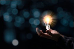 Two hands holding the light bulb that is illuminating. Creative protecting patents and ideas concept.