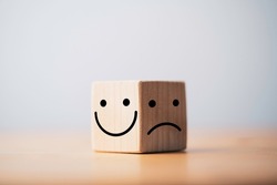 Smile face in bright side and sad face in dark side on wooden block cube for positive mindset selection concept.