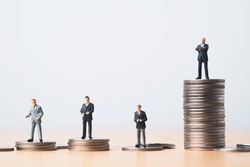Miniature figure of four businessmen standing to different high and low coins stacking for position and successful business investment income concept.