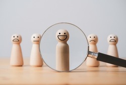 Smile face of wooden figure inside of magnifier glass among sad face for customer focus and relation management , excellent evaluation after client use product and service concept.