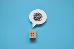 A wooden cube with a sad face with a tangle of thoughts in its head. A person can't collect his thoughts