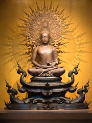 Golden Buddha sculpture in lotus position sitting on an orange background