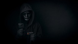 Dangerous anonymous hacker man in hooded and mask use smartphone and credit card, break security data and hack password with personal data Bank account. Internet crime, cyber attack security concept
