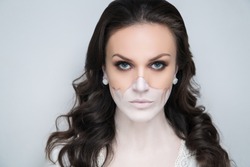 Half of female face is shaded with beige foundation, drains to cheeks. White chin and neck painted with light paint, bleached body. Mask conceptual make-up, intensive eye shadows, long black eyelashes