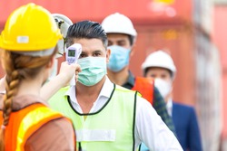 Female worker scanning fever temperature with digital thermometer to construction site staff wearing hygiene face mask protect from Coronavirus or COVID-19. New Normal working life adaptation in 2020