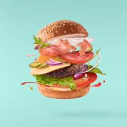 Delicious burger with flying ingredients isolated on turquoise background