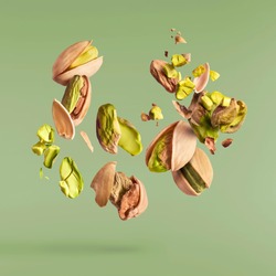 Flying in air fresh raw whole and cracked pistachios  isolated on green background. Concept of Pistachios is torn to pieces close-up. High resolution image