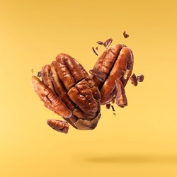 Fresh tasty pecan nuts falling in the air isolated on yellow background. Food levitation concept. High resolution image.