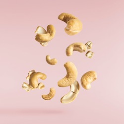 Fresh tasty Cashew nuts falling in the air isolated on pink background. Food levitation concept. High resolution image.