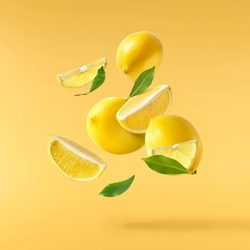 Fresh raw lemons with green leaves falling in the air isolated on yellow illuminating background. Food levitation or zero gravity conception. High resolution image