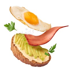 Fresh delicious tasty homemade sandwich with avocado, roasted egg and bacon falling in the air isolated on white background