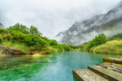 wooden bridge over turquoise water of a river in the mountains in the rain, gertrude valley lookout, southland, new zealand