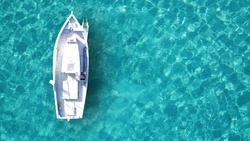 Aerial drone bird's eye top view of white traditional fishing boat in turquoise clear waters, Cyclades, Greece