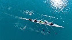 Aerial drone bird's eye view of sport canoe operated by team of young men in emerald clear sea