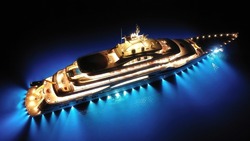 Aerial drone night shot with copy space of beautiful latest technology modern led illuminated luxury mega yacht anchored in tropical exotic bay with deep blue sea