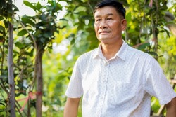 Portrait close-up shot of middle-aged Asian male model with short black hair wearing a white shirt with stand smiling in the garden