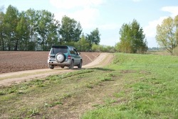 the green car is driving on the road in the field in summer