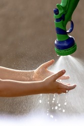 A child washing his hands in a hose of gushing water. Fresh spring water gushes from a hose in the hands of a child.
