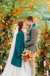 Newlyweds under the arch of interwoven branches with yellow leaves in autumn park