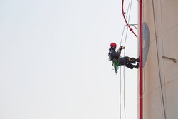 Male worker rope access industrial working at height tank oil wearing harness, helmet safety equipment rope access inspection of thickness tank oil and gas.