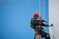 Closeup male workers control swing rope down height tank rope inspection of thickness scan tank gas background blue sky.