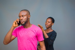 a young African man angrily making a call with a lady behind trying to talk to him
