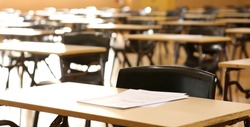 A high school hall or room set up ready for an end of year final exam to be sat by students. examination paper sitting on the edge of a desk or table. 