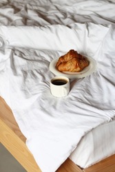 Cozy bedroom with cup of coffee and croissants on a white bed. Concept of breakfast and coziness at home.