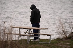 unknown man stands alone at the lake and watches the water