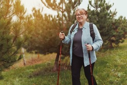 Outdoor activities, people and vacations concept. Attractive short haired middle aged woman in activewear hiking in forest using poles for nordic walking, doing aerobic workout, enjoying nature