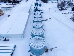Aerial photo of multiple snow covered agricultural grain bins and grain elevator in rural North Dakota town, winter. Snow, farm industry.