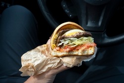 A person eats a double patty cheeseburger ordered from a drive-through burger chain restaurant in his car. Dangerous forever chemicals are said to be found in wrappers at major fast food restaurants.