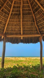 Vertical view of the beach and the sea through a hut made of wooden logs and palms