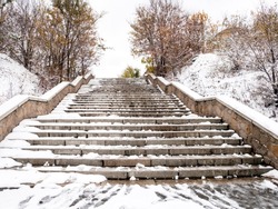 Stone concrete snow-covered stairs with footprints in the city in late autumn or winter. Stairway to heaven.