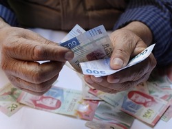 hands of an elderly man holding and counting mexican banknotes