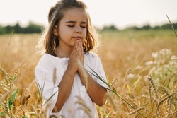 Little Girl closed her eyes, praying in a field wheat. Hands folded in prayer. Religion concept