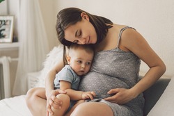Young woman with her first child during second pregnancy. Motherhood and parenting concept. Toddler boy and mom. Happy family expecting for baby. 