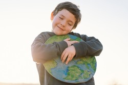 Protection and love of earth. Little boy holding planet in hands against green spring background. Earth day concept. Environmental Conservation