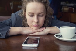 Disappointed sad woman looking at phone and waiting message or call