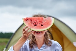 Funny woman eating watermelon on a picnic. Girl closed her eyes with a watermelon, looking into the holes.