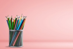 Classic art colored pencils in a bucket on a pink background.