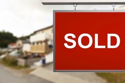 Estate agent SOLD sign with the defocussed street of houses in the background