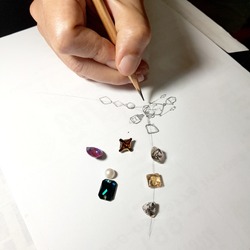 Jewelry designers are painting the necklace with a pencil on a piece of paper before the model can be produced.