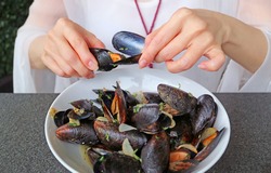 Woman Having her Steamed Mussels in White Wine by Using an Empty Mussel Shell to Grab Another Mussel's Meat Out